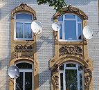 101_9213 Die Fenster des Wohnhauses in der Wilhelmsburger Strasse Vogelhttendeich sind mit farblich abgesetzten Jugendstil- Dekoren eingefasst. Die Hausfassade ist mit gelb- weiss glasierten Ziegeln verkleidet. An den Fenstern des Hauses sind mehrere Satellitenschsseln angebracht. www.bilder- hamburg.de
