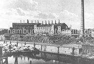 79_0247 Historisches Foto aus Hamburg Wilhelmsburg ca. 1920 - am Ufer des Veringkanals sind Baumstmme gestapelt; an den Kaianlagen liegen Schuten, die ebenfalls hoch mit Baumstmmen beladen sind. Im Hintergrund Fabrikgebude und Schornsteine.  www.hamburger-fotoarchiv.de