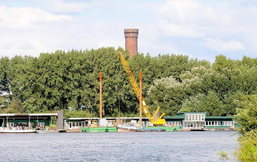 01137_8360 Blick ber die Norderelbe zu den Pontons in Hamburg Entenwerder - Holzhuser, Arbeitsbuden stehen auf den schwimmenden Anlegern, ein Schwimmkran und Barkassen / Schuten haben dort festgemacht. Hinter den Bumen vom Elbpark Entenwerder die Spitze vom Wasserspiel / Wasserturm Hamburg Rothenburgsort. 