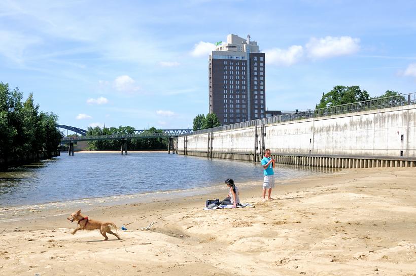 01169_5759 Das stillgelegte Hafenbecken HAKEN in Hamburg Rothenburgsort wurde teilweise mit Sand verfllt - Einwohner nutzen die Anlage als Strand - ein Hund spielt am Wasser. Im Hintergrund die Fussgngerbrcke vom Alexandra-Stieg und das Hochhaus vom Hotel Holiday Inn.