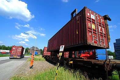 011_15722 - dann wird der Container vorsichtig abgesenkt, um seinen exakten Platz auf dem Wagen zu finden; lks. im Hintergrund transportiert ein Lastwagen einen Container.