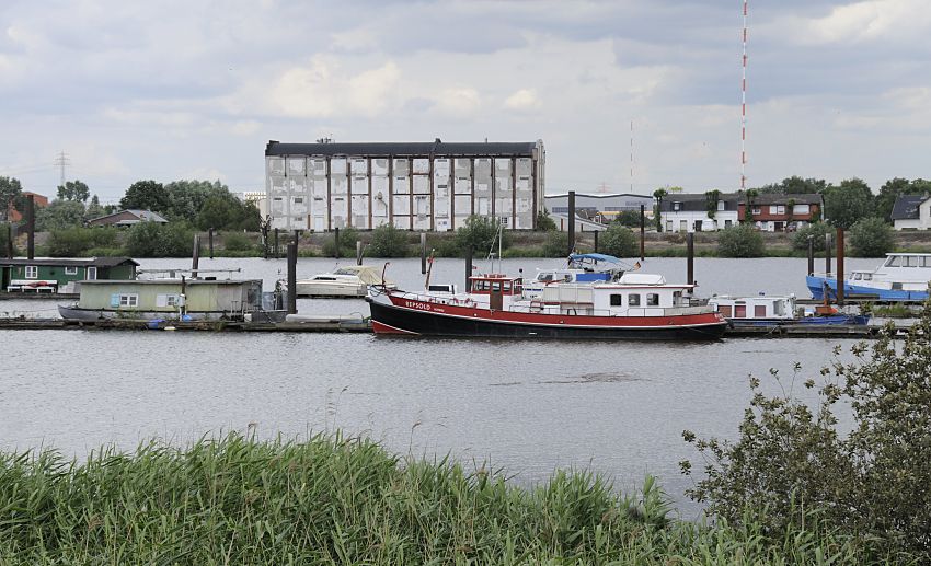 11_17526 Blick ber den Holzhafen in Hamburg Moorfleet - auf der gegenber liegendes Seite der Moorfleeter Deich und die typische Industriearchitektur eines Lagergebudes. An den Bootsstegen des ehemaligen Laufs der alten Doveelbe sind Boote vertut. 