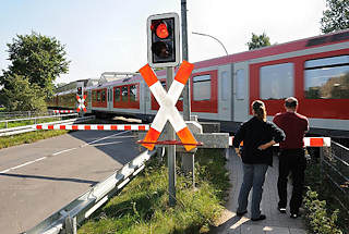 8390 Bahnbergang Hamburg Sllfeld. Die BAhnschranken sind heruntergelassen - ein Zug der Hamburger S-Bahn fhrt Richtung Wedel vorbei.