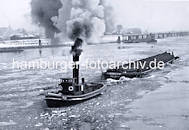 1079_33_18 Ein Schlepper fhrt unter Dampf im Treibeis auf der Elbe - das Arbeitsschiff mit hohem Schornstein zieht  eine abgedeckte Schute, zwei Schiffer stehen am Heck des Kahns. Am Ufer sind die Zollanlagen von Hamburg Entenwerder zu erkennen.  