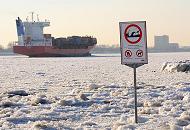208_5784 Zwischen dem Eis steht am Elbstrand ein Warnschild, das auf Wellenschlag und Sog sowie auf die Gefahr des Ertrinkens hinweist. Der Container Feeder NAVI BALTIC hat den Hamburger Hafen verlassen und fhrt elbabwrts durch das Treibeis. 