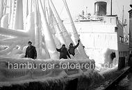 219_8_83 Die Mannschaft eines norwegischen Frachters, der gerade im Hamburger Hafen eingetroffen ist, steht an Deck des stark mit Eis bedeckten Schiffs. Die Decksaufbauten und Takelage des Frachtschiffs sind mit einer sehr dicken Eisschicht berzogen. 