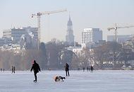 237_5509 Ein sonniger Winternachmittag in Hamburg - Spaziergnger genieen das schne Winterwetter und gehen auf der zugefrorenen Alster spazieren. Eine Mutter luft auf dem Eis der Alster Schlittschuh und zieht dabei ihr Kinde auf einem Schlitten. Im Hintergrund der Turm der St. Michaeliskirche.