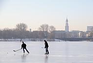 241_5574 Jugendliche spielen Eishockey auf der zugefrorenen Alster - hinter der Kennedybrcke sind die Huser am Jungfernstieg zu erkennen und der Kirchturm der St. Michaeliskirche.