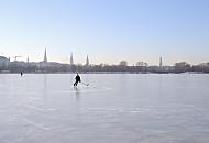 242_5558 Ein Eishockeyspieler dreht einsam seine Kurven auf dem Alstereis. Im Hintergrund das Panorama von Hamburg mit den Trmen der Hansestadt.