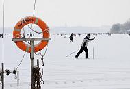 244_6093 Vor dem Anleger des Bootssteg vom Alstercaf Bobby Reich luft ein Hamburger Ski auf der zugefrorenen und verschneiten Alster; ein verschneiter Rettungsring hngt am Steg in seiner Halterung.