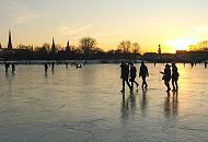 257_5875 Spaziergnger dem Eis der zugefrorenen Alster gehen Richtung Hamburg - St. Georg. Das Licht der untergehenden Sonne spiegelt sich auf der blanken Eisdecke.