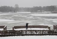 268_5042 An einem grauen Wintertag geht ein Paar am Stadtparksee spazieren - sie schtzen sich mit einem Schirm gegen den Schneefall. Auf dem fast zugefrorenen See sitzen Mwen auf dem dnnen Eis. Im Hintergrund das Freibad Stadtparksee.
