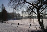 280_1010042 Der Jogger, der an einem Wintermorgen um den See des Hamburger Stadtparks joggt, wirft einen langen Schatten auf den Schnee. Ein anderer Stadtparkbesucher steht in der Sonne am Ufer und geniet den Blick auf den zugefrorenen See in der Sonne.