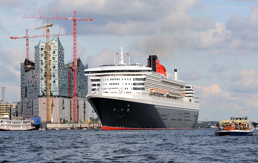 8550 Die Queen Mary verlsst den Hamburger Hafen - das Kreuzfahrtschiff hat vom Kreuzfahrtterminal Hafencity abgelegt und fhrt Hhe Elbphilharmonie. Touristen an Bord einer Barkasse der Hamburger Hafenrundfahrt beobachten das Auslaufen des grossen Kreuzfahrtschiffs.
