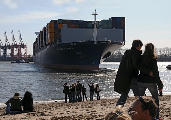 11_17453 - Ein Containerriese wird bei Oevelgoenne von Schleppern in den Waltershofer Hafen gezogen - am Burchardkai wird der Frachter dann entladen.  Bei der Strandperle sitzen die Gste im Sand oder stehen in der Sonne am Elbufer und beobachten das Geschehe.