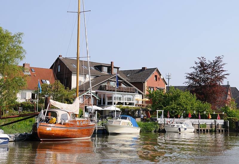 Fotos vom Hamburger Ausflugsziel - Altes Land / Cranz. Sportboote am Ufer der Este bei Hamburg-Cranz.  036_7450 Die Este ist ein reizvolles und interessantes Sportbootrevier. Viele Anwohner haben ihre Schiffe am Ufer liegen und fahren mit ihren Booten auf  der naheliegenden Elbe. Ein Holzsegelschiff und Sport-Motorboote liegen am Ufer der Este - im Hintergrund die Terrasse eines Cafs am Wasser.