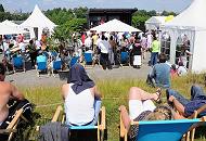 58_9317 Wilhelmsburger und Bürger der Veddel hören der Rede zu die die Politiker anlässlich der Zollzaunöffnung am Spreehafen halten. Einige sitzen in Liegestühlen auf dem Deich in der Sonne. 