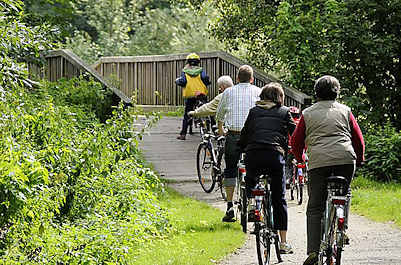 11_21555 Eine Familie macht auf dem Billewanderweg eine Fahrradtour. Eine Holzbrücke führt die Fahrradfahrer und Fahrradfahrerinnen über den Hamburger Fluss.