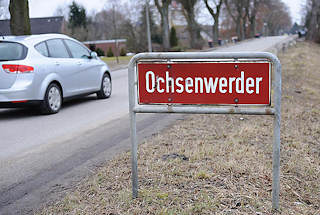 0509 Bilder aus dem Hamburger Stadtteil Ochsenwerder - Bezirk Hamburg Bergedorf. Rotes Stadtteilschild mit weisser Schrift an der Strasse.
