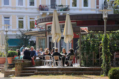 8103 Strassencafe in der Sonne - Gäste sitzen in Hamburg Ottensen an der Eulenstrasse.