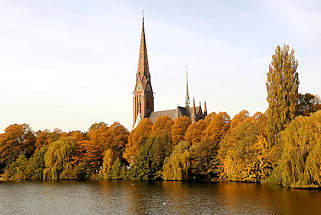 0061 Herbstbäume am Ufer des Kuhmühlenteichs in Hamburg Uhlenhorst - herbstlich gefärbte Blätter - Kirchturm der St. Gertrudenkirche.