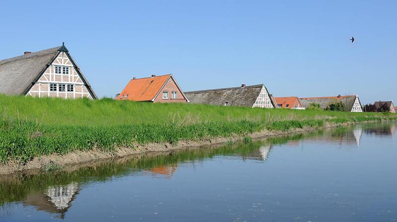 Bilder vom Alten Land; Hamburger Ausflugsziel am Wochenende. Fachwerkhuser hinter dem Deich an der Lhe. 021_4078 Bauernhuser und Wohnhuser sind mit einem Deich vor der berflutung durch Hochwasser der Lhe geschtzt.  Historische reetgedeckte Fachwerkhuser und Klinkerhuser stehen entlang des 12,7 km langen Flusses des Alten Landes. Die Giebel der Huser spiegeln sich im ruhigen Wasser.