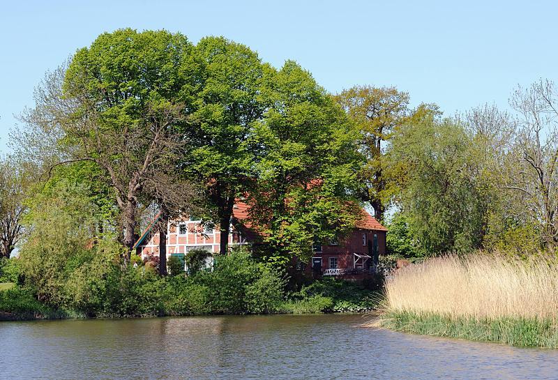 Frhling im Alten Land - Wasserweg LHE. Alte Bume am Flussufer - Fachwerkhaus mit Dachziegeln gedeckt. 022_4136 Ein historisches Fachwerkhaus steht inmitten hoher Bume am Ufer der Lhe. Die meisten Bume tragen das frische Grn des Frhlings - andere haben noch kein Blattwerk.