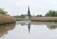 057_7471 Die Este ist von der Mndung fr Sportboote je nach Tide schiffbar. Das Flussufer ist kurz vor Buxtehude mit dichtem Schilf und Gras bewachsen. Der hohe Turm der Buxtehuder St. Petrikirche spiegelt sich im Wasser des ruhigen Flusses.