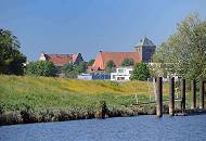 073_4791 Blick vom Flusslauf der Schwinge zur Stadt Stade; alte Eisenpoller am Ufer der Schwinge zeugen von dem ehemaligen Wirtschaftsverkehr, der auf der Fluss stattgefunden hat. Am Deich des Flusses blhen gelbe Blumen - im Hintergrund die dreischiffige gotische Hallenkirche St. Wilhadi.