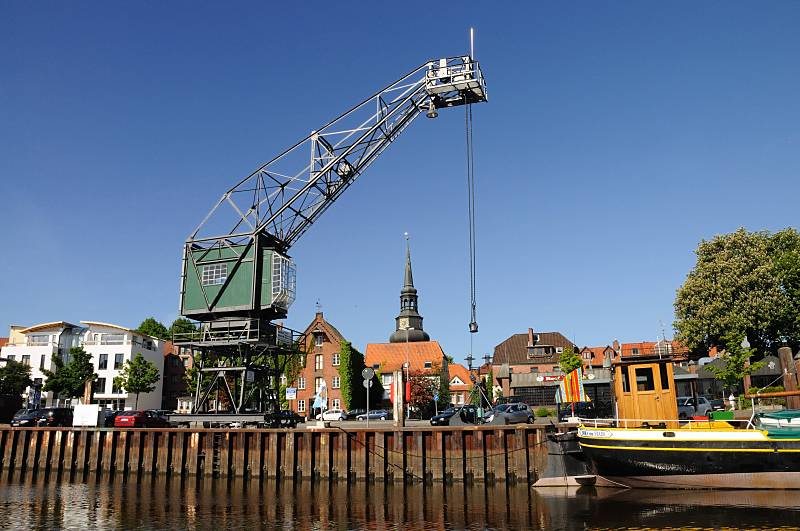 Kran am Ufer des Stader Hafens, Traditionsschiff Dora von Stade - Wohnhuser + Kirchturm. Tourismus in der Metropolregion Hamburg / Hansestadt Stade. 083_8073 Hafenkai von Stadt, ein Rollkran steht am Hafenrand; im Hintergrund Wohnhuser und ehemalige Speichergebude. Rechts das Heck mit der Ruderanlage des 1902 in Itzehoe gebauten und jetzt restaurierten Kstenfrachters "DORA VON STADE".