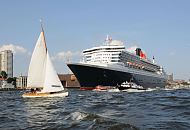 09_4392 Die Queen Mary 2 auf der Elbe vor Hamburg Neumühlen, viele Schiffe begleiten das riesige Passagierschiff; eine Segelyacht kreuzt vor dem Bug des Kreuzfahrtschiffs. Die R.M.S. (Royal Mail Ship)  Queen Mary 2 (QM2) ist mit 148.528 BRZ eines der größten Passagierschiff der Welt. Das britische Kreuzfahrtschiff  hat eine Länge von 345 m und eine Breite von 45 m. Der Luxusliner bietet in 1310 Kabinen bis zu 2.620 Passagieren Platz und hat eine Besatzung von 1.253 Personen. Die Queen Mary 2 hat fünf Swimmingpools, einen Ballsaal, Golfanlage, Wintergarten, Sportzentrum, mit über 8.000 Büchern die größte Bibliothek auf See, den größten öffentlichen Saal (Restaurant Britannia), der über zwei Decks und die gesamte Schiffsbreite geht, acht weitere Restaurants, Fitness-Center, Planetarium, Kino, Theater.  ©www.fotograf- hamburg.de