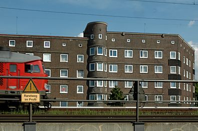 011_14321 - rote Lokomotive fhrt entlang der Wohnhuser auf der Veddel; Schildaufschrift " Randweg im Profil " (was immer das auch heissen mag)